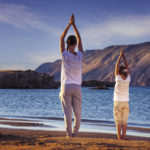 Mother and daughter, yoga on the beach early in the morning